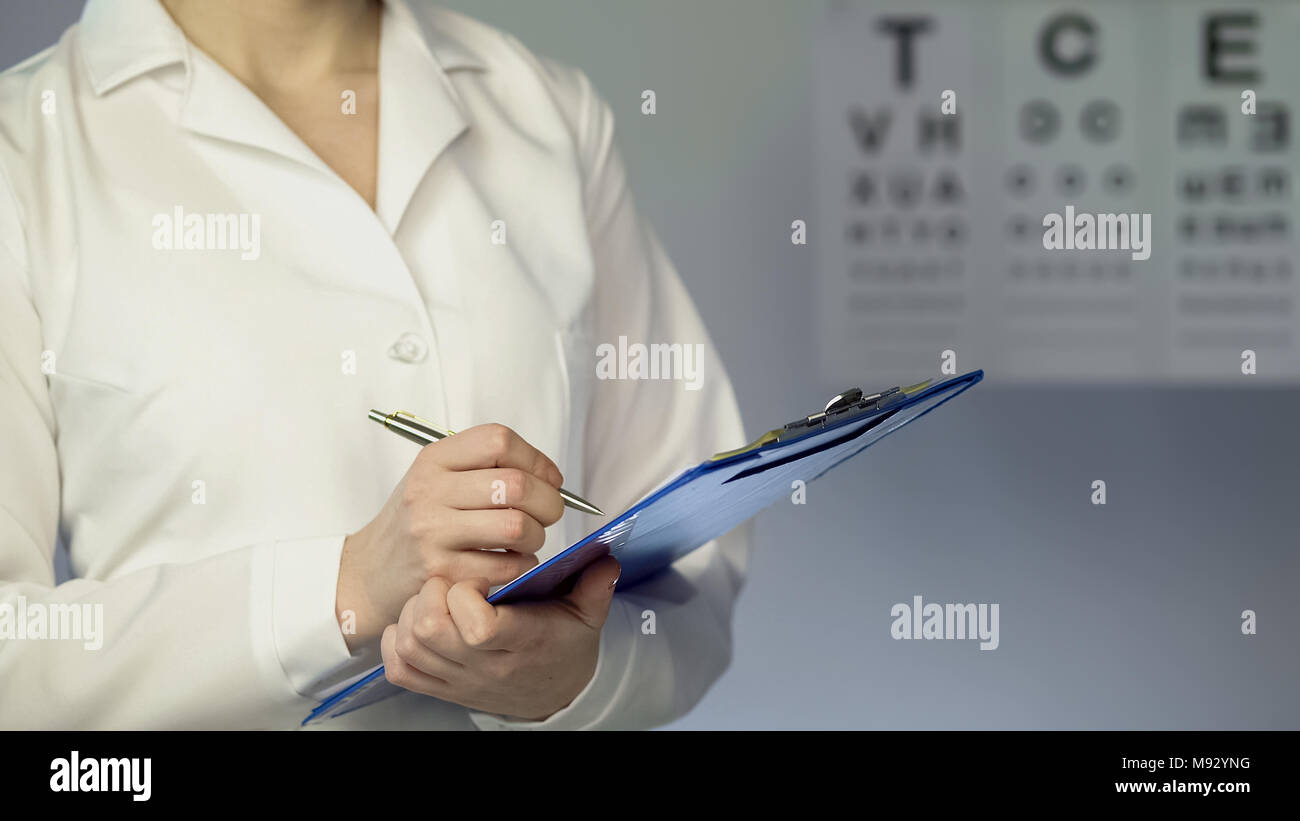 Female ophthalmologist writing down patient diagnosis and treatment, examination Stock Photo