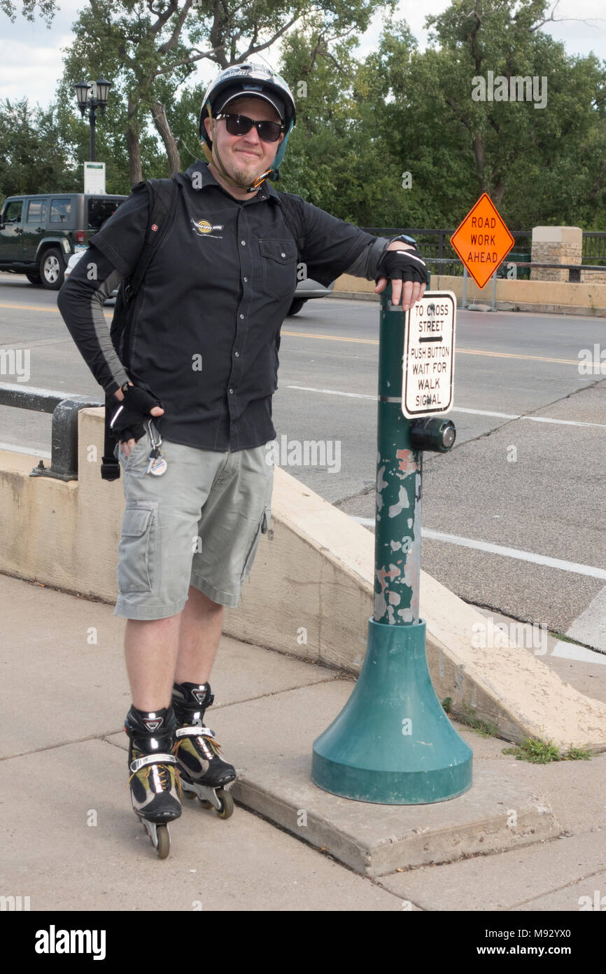Happy-go-lucky man on rollerblades resting on poll with button and instructions for safely crossing street. Minneapolis Minnesota MN USA Stock Photo