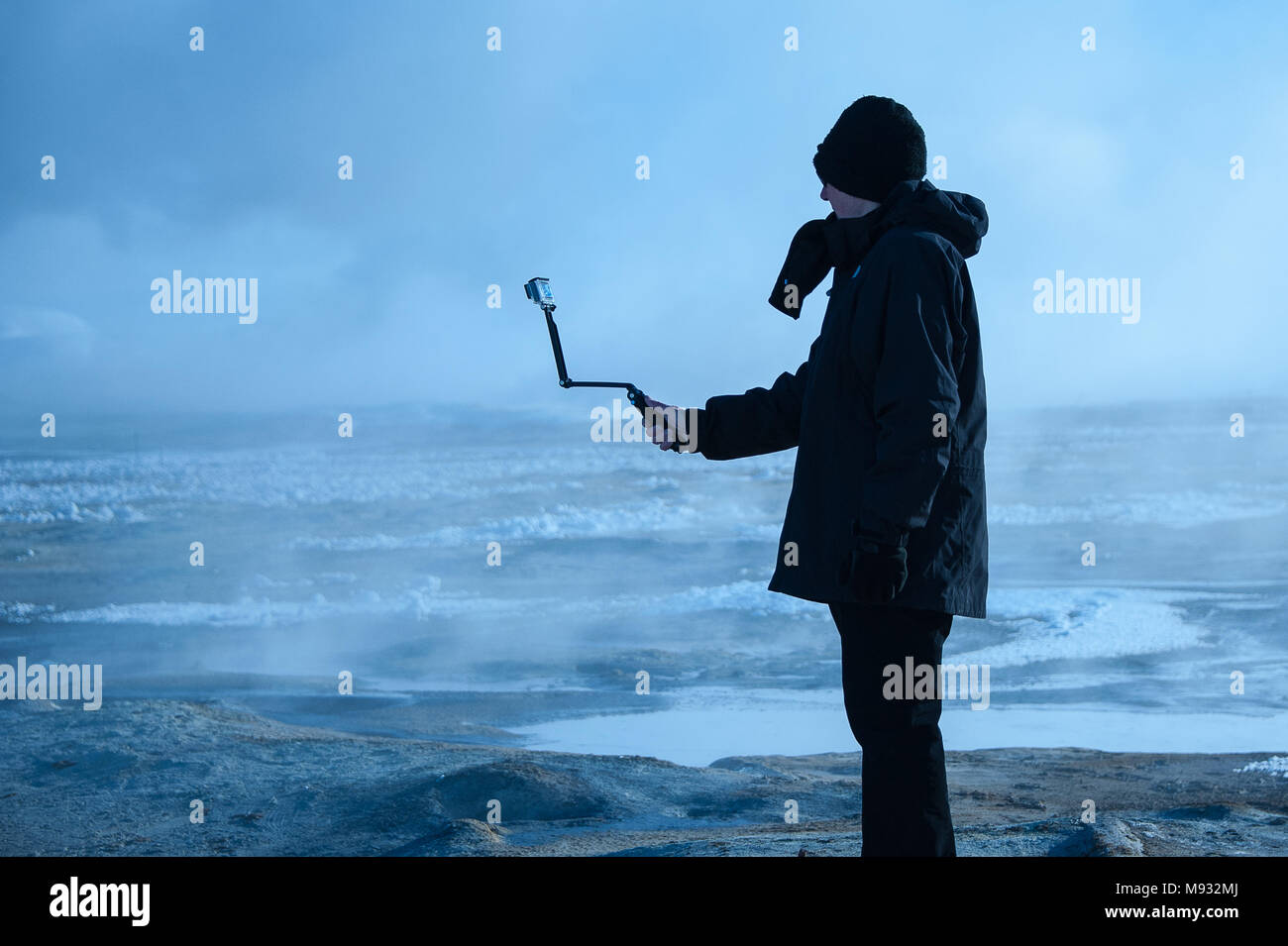 Namafjall geothermal fields, Iceland - March 2016: Man taking pictures with camera on selfie stick, surrounded by steaming, sulphurous mudpots Stock Photo