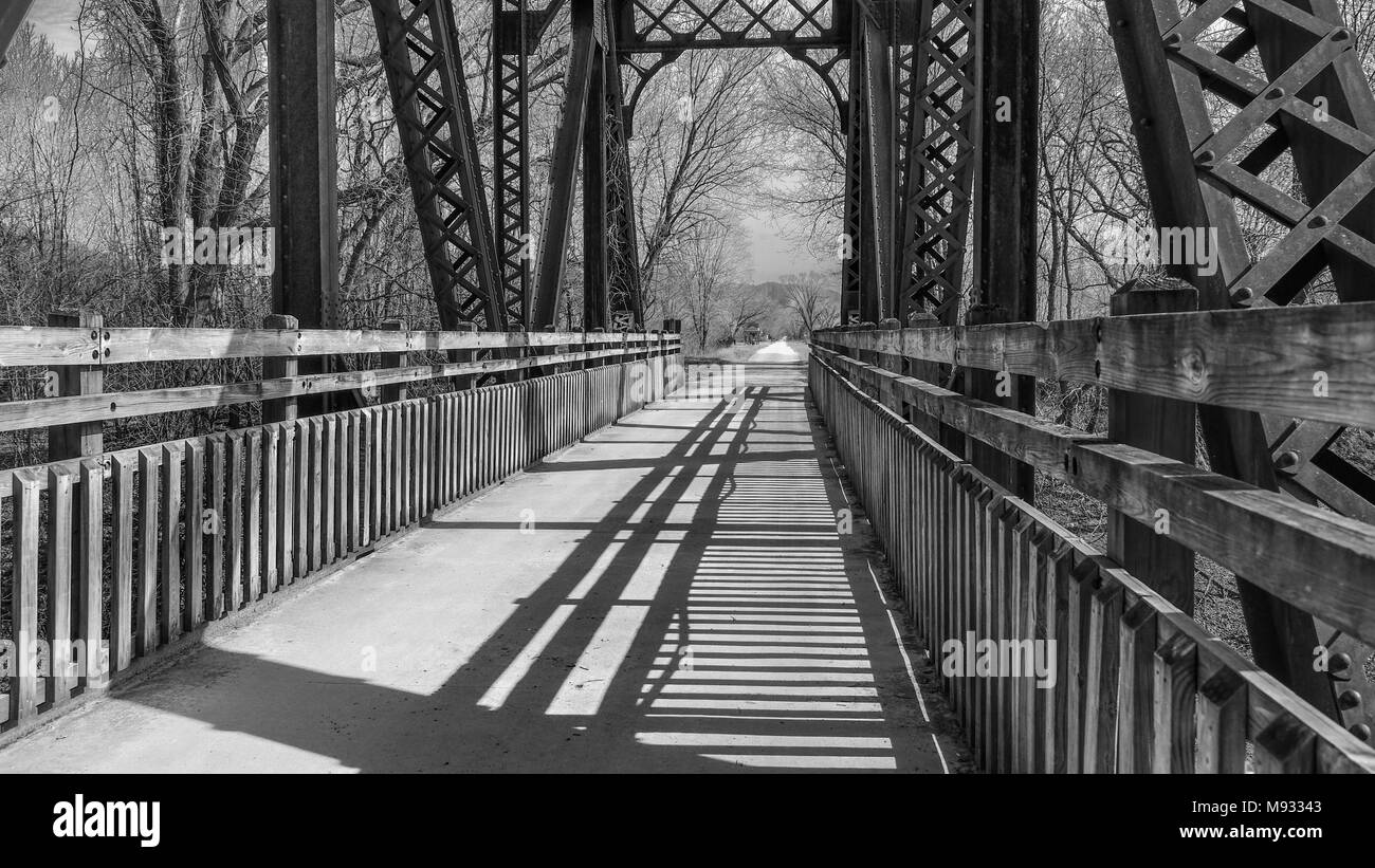 View of an old railroad bridge converted into a park trail in late afternoon in black and white, long shadows on the right; Missouri, Midwest Stock Photo