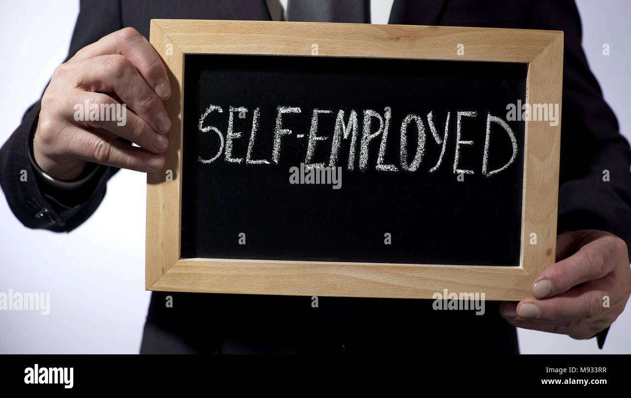 Self-employed written on blackboard, businessman holding sign, business concept Stock Photo