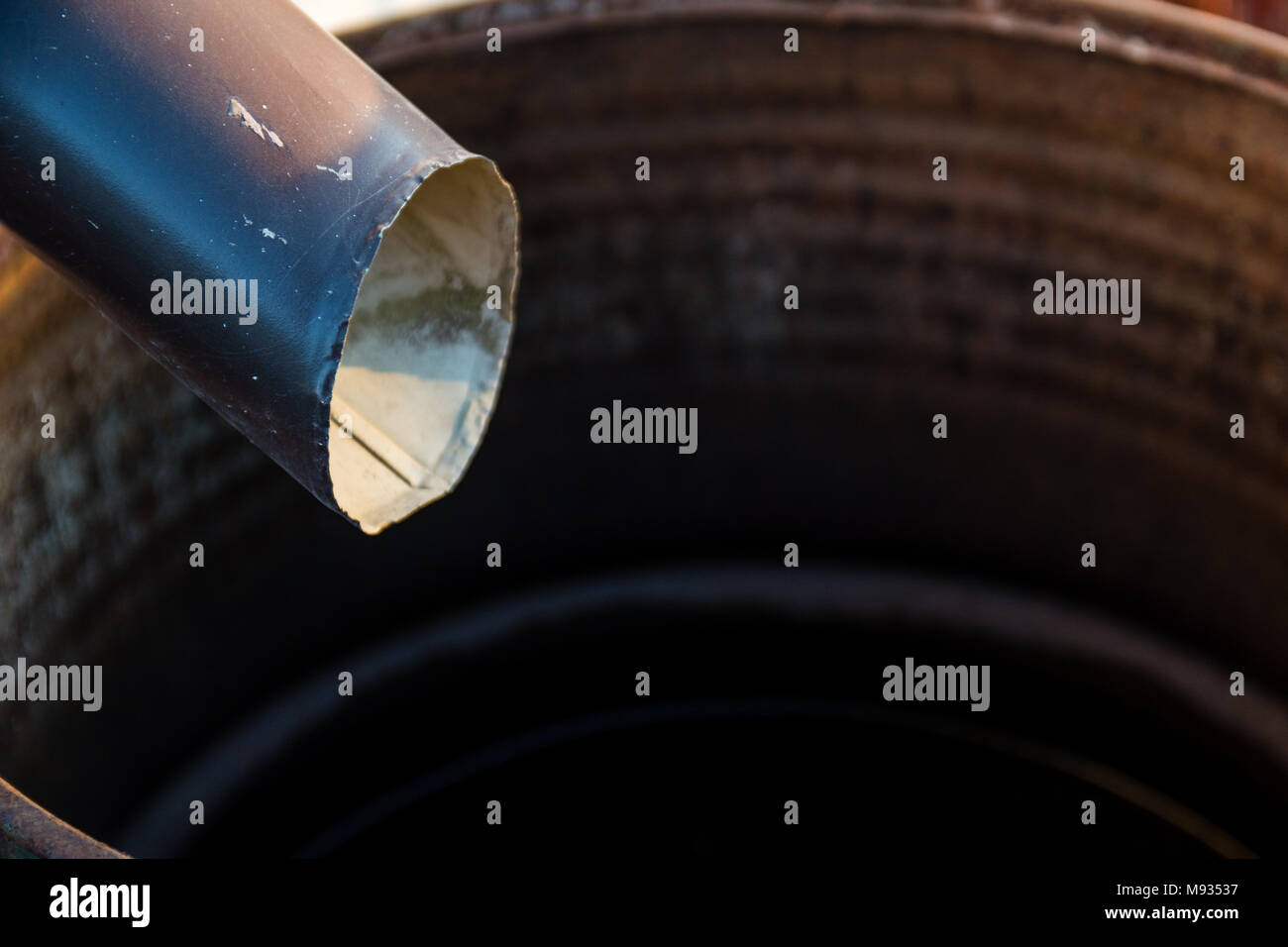 Black metal gutter downspout draining into rain barrel on sunny day in