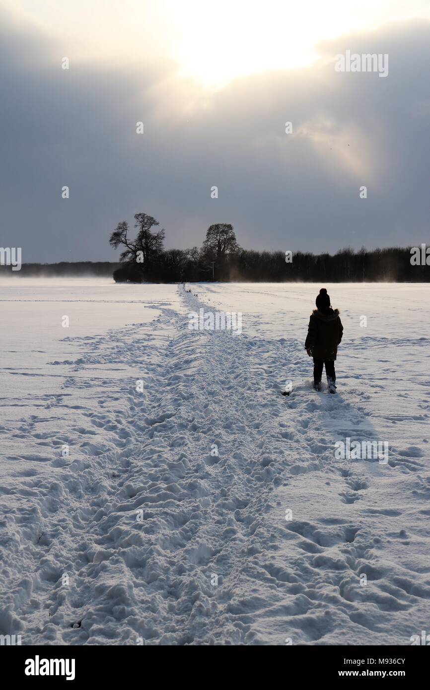 A small figure silhouetted on a snowy path across fields Stock Photo