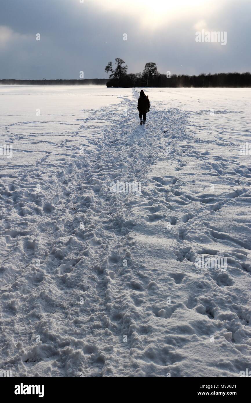A small figure silhouetted on a snowy path across fields Stock Photo