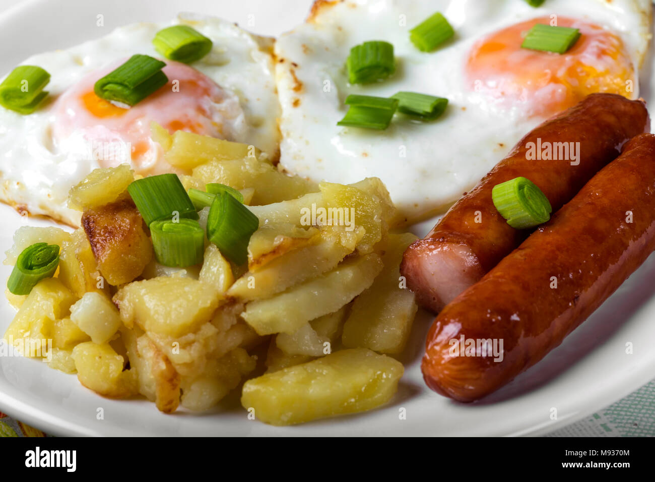 Close up of eggs with fried potatoes and sausages with pieces of green