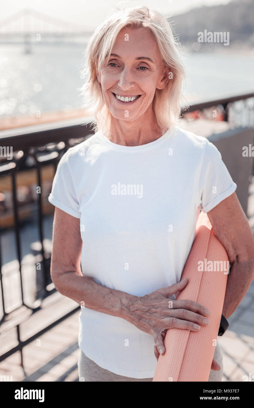 Joyful gray haired woman holding gum rug and smiling. Stock Photo