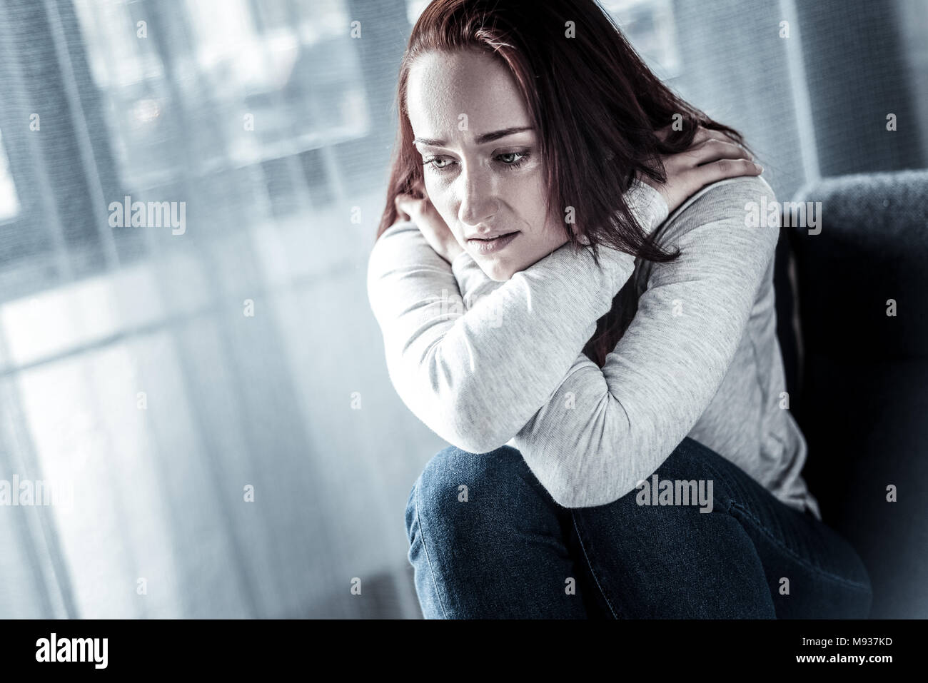 Stressful unhappy woman hugging herself and looking down. Stock Photo