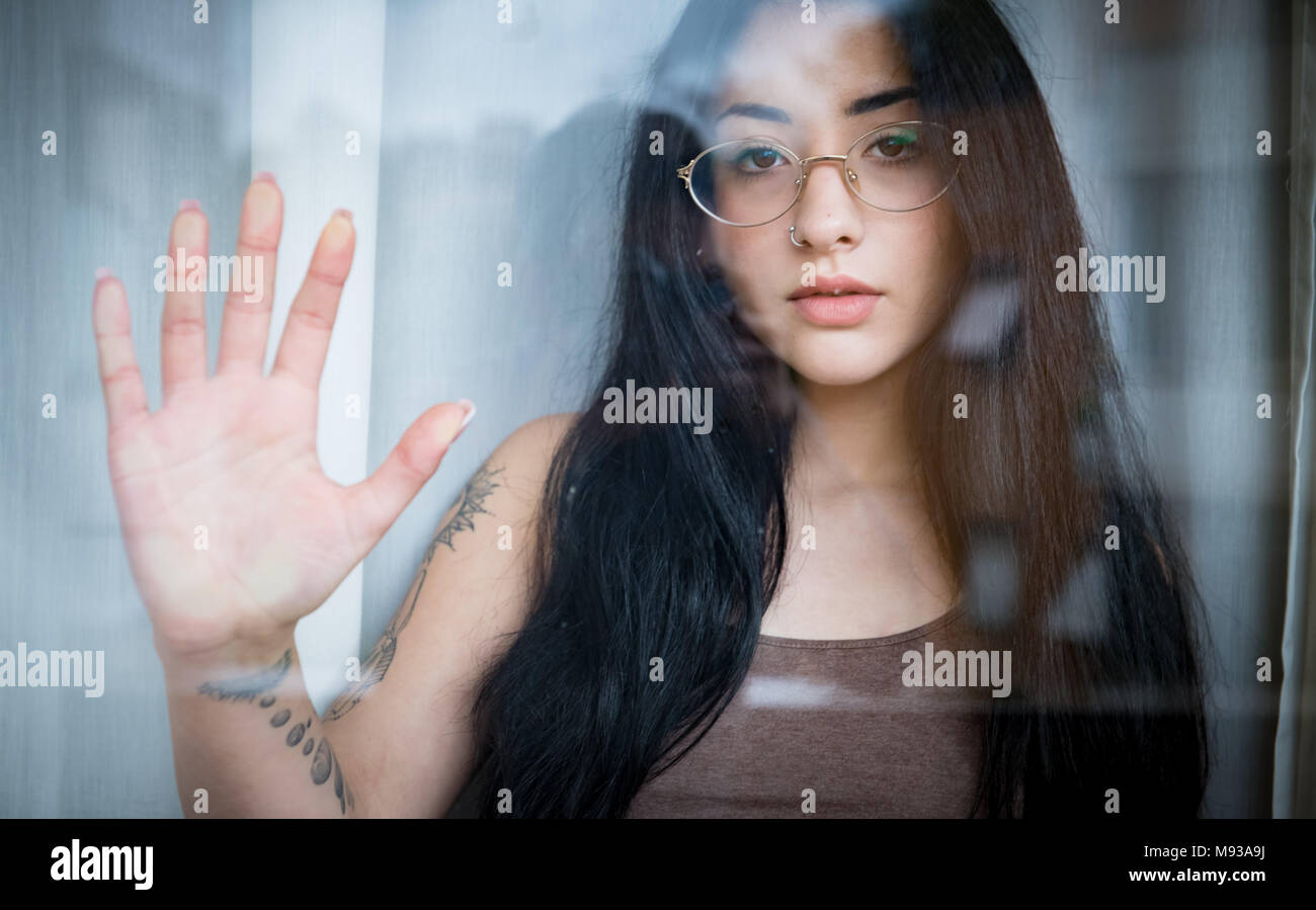 Pretty girl female teenager behind window hand up looking at camera Stock Photo