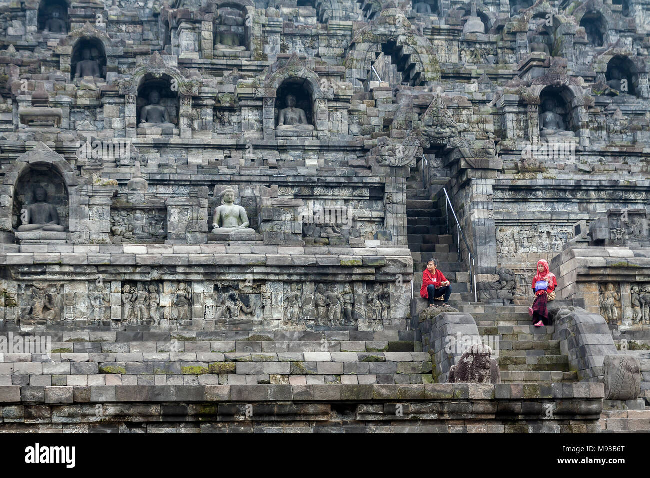 Sense of Scale with two young girls waiting amongst Buddha statues at the World Famous tourist attraction and Unesco site of Borobudur Buddhist temple Stock Photo