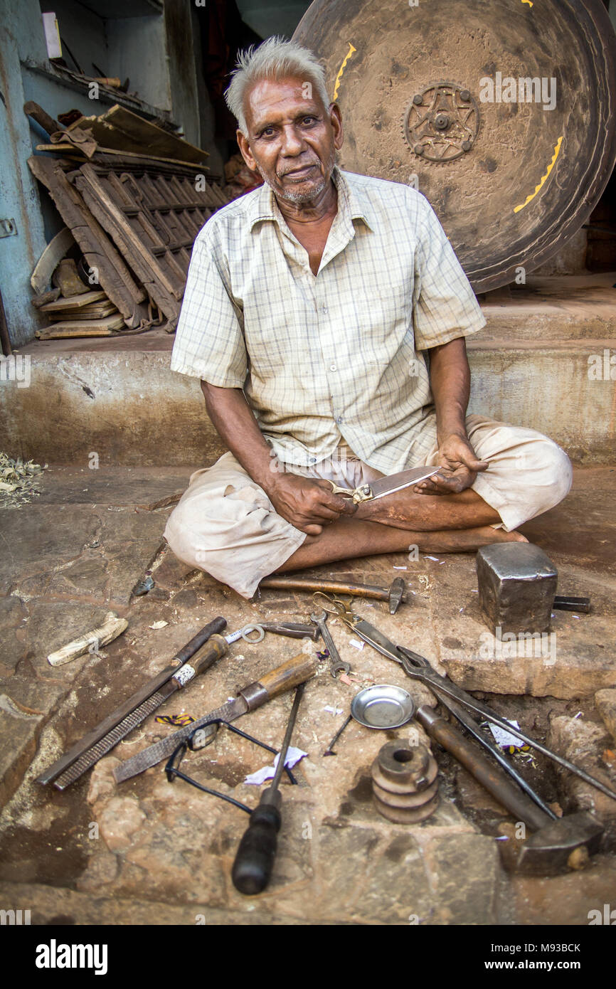 Portrait of skilled man with tools of the trade laid out before him as he sits in front of his knife sharpener, a huge wheel primitive sharpening tool Stock Photo