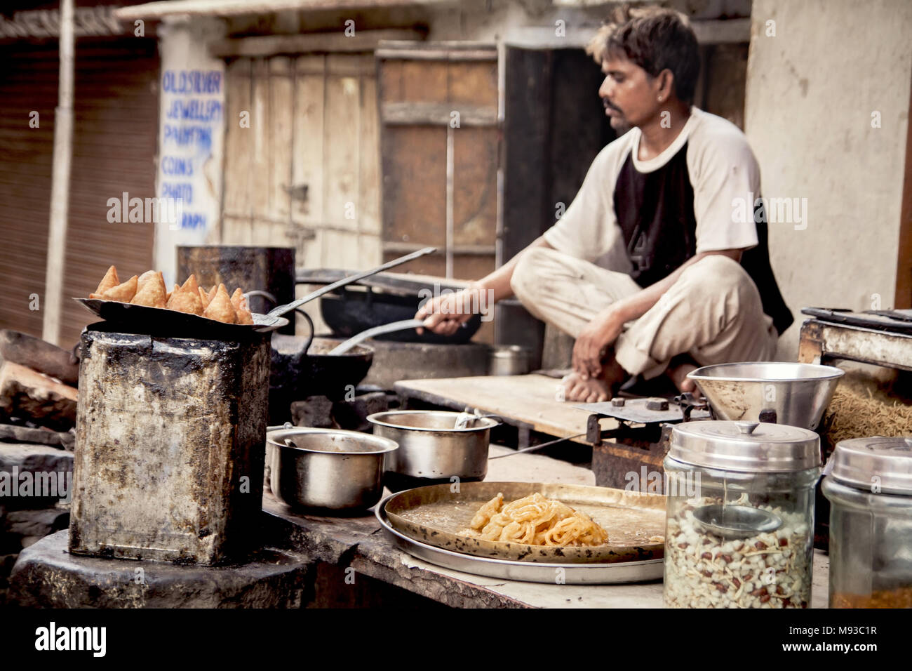 Seated Indian man cooking deep fried Samosa on street stall. Samosa in India are a quick and easy delicious and appetising form of street food. Stock Photo