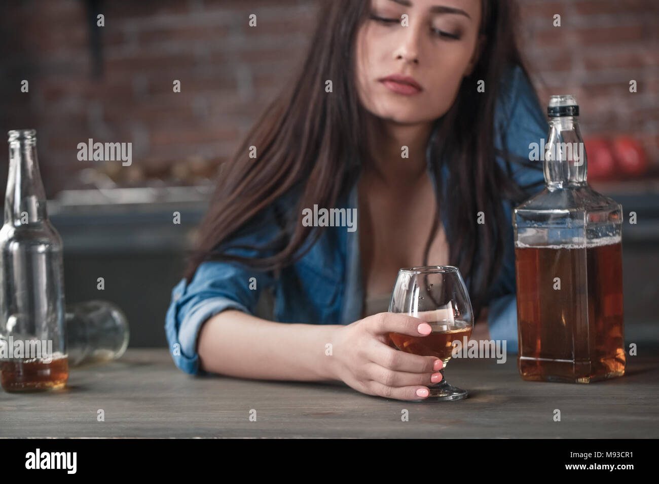 Young female alcoholic social problems sitting at table drinking whiskey holding glass looking down upset close-up Stock Photo