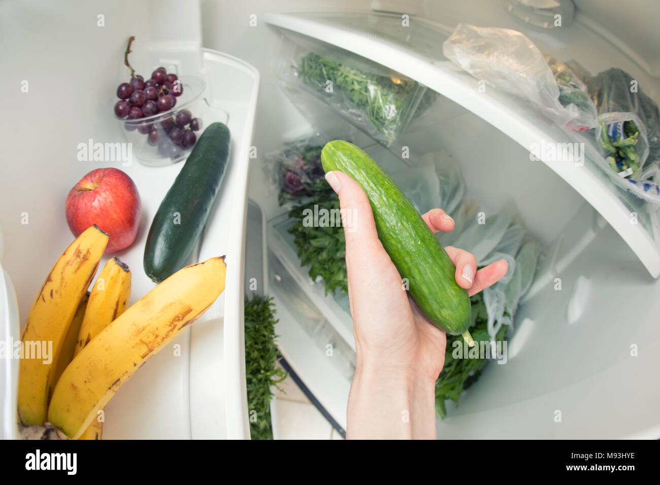 Healthy diet: A hand grabbing a cucumber from the open refrigerator full of greens. Stock Photo