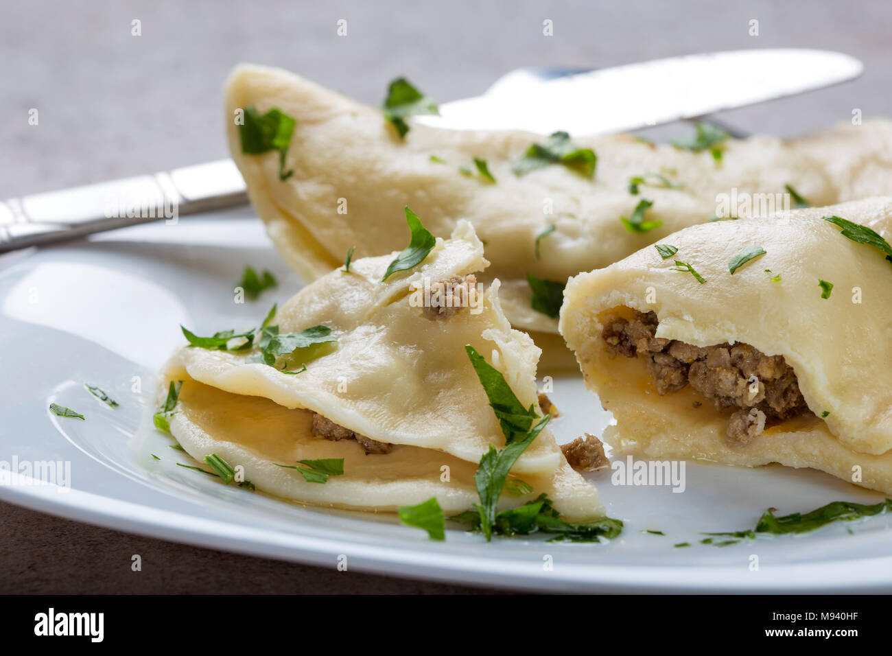 Pierogi, pyrohy or dumplings, filled with beef meat and covered with parsley on plate with knife Stock Photo