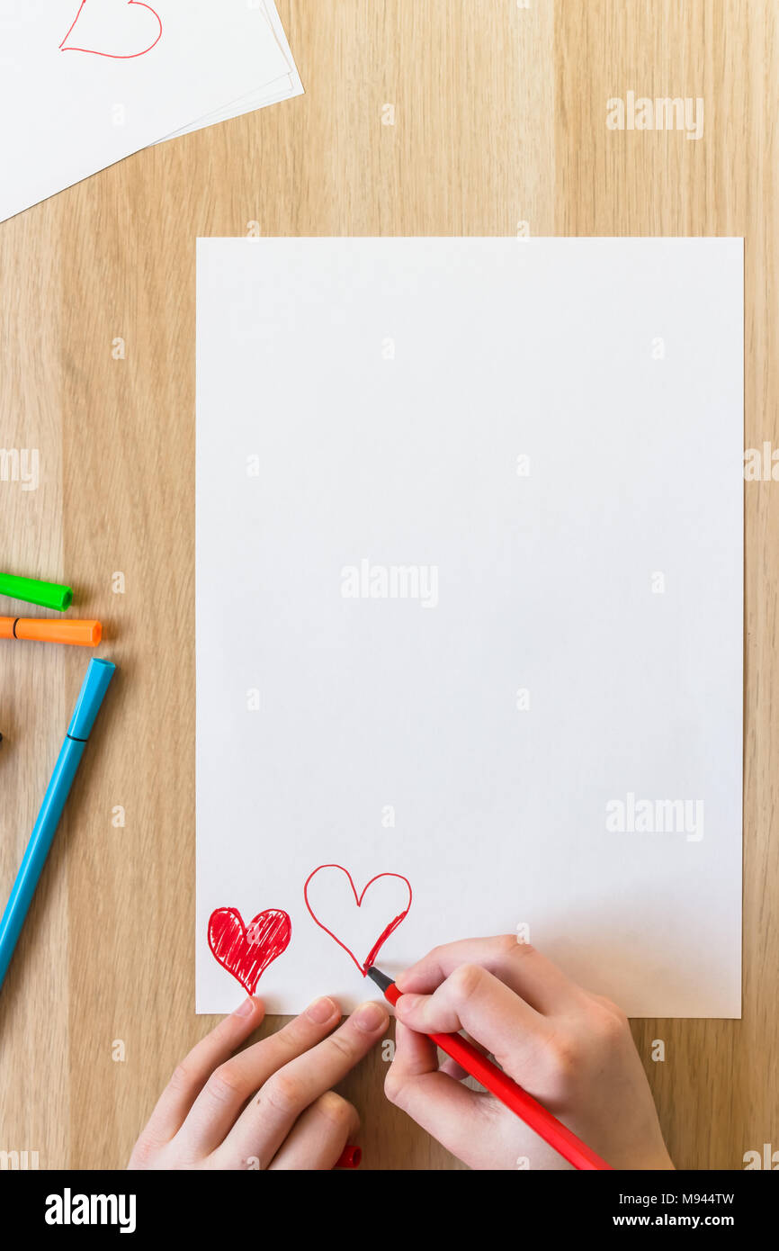 A hand is drawing red hearts on white paper Stock Photo