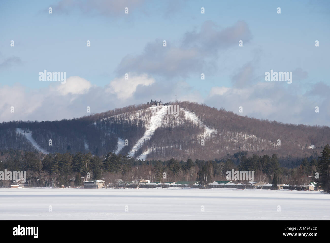 A view of Oak Mountain Ski Hill from Lake Pleasant in the Adirondack Mountains, NY with snow, ice, a blue sky background and copy space. Stock Photo