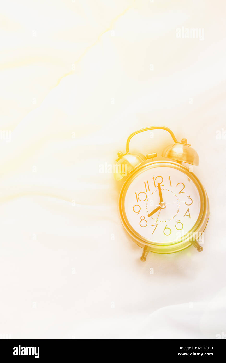 Alarm Clock Showing Eight O'Clock Lying on White Bed Blanket in Bedroom. Bright Golden Morning Sunlight Streaming Through Window. New Day Beginning Wa Stock Photo