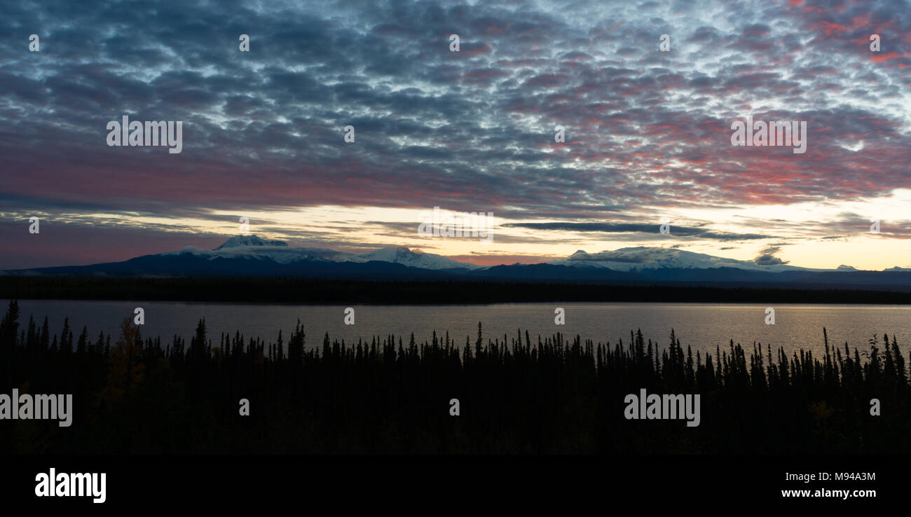 The sun sets reflecting light into the clouds above Willow Lake outside Wrangell St-Elias National Park Stock Photo