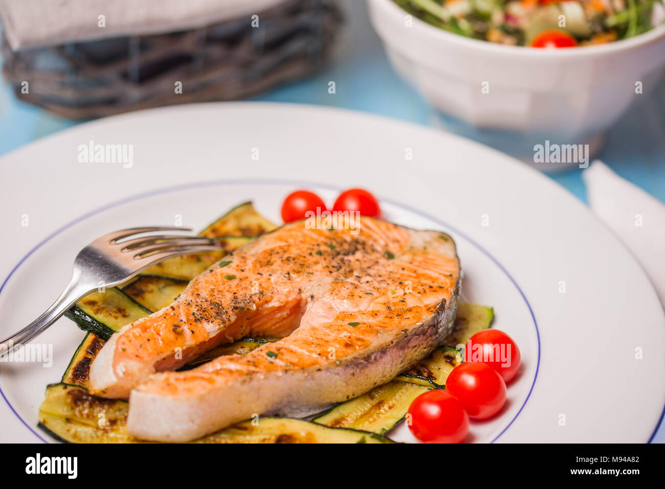 Roasted salmon and green zucchini with vvegetables salad in background Stock Photo