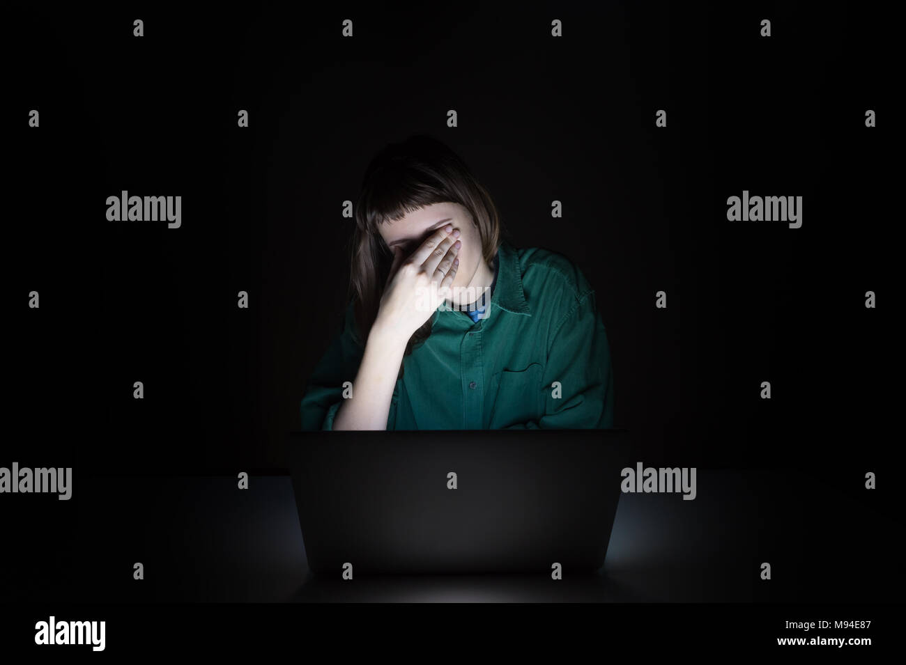 Tired and exhausted young woman rubs eyes at laptop pc late in the evening. Portrait of depressed female student or worker sitting in front of compute Stock Photo