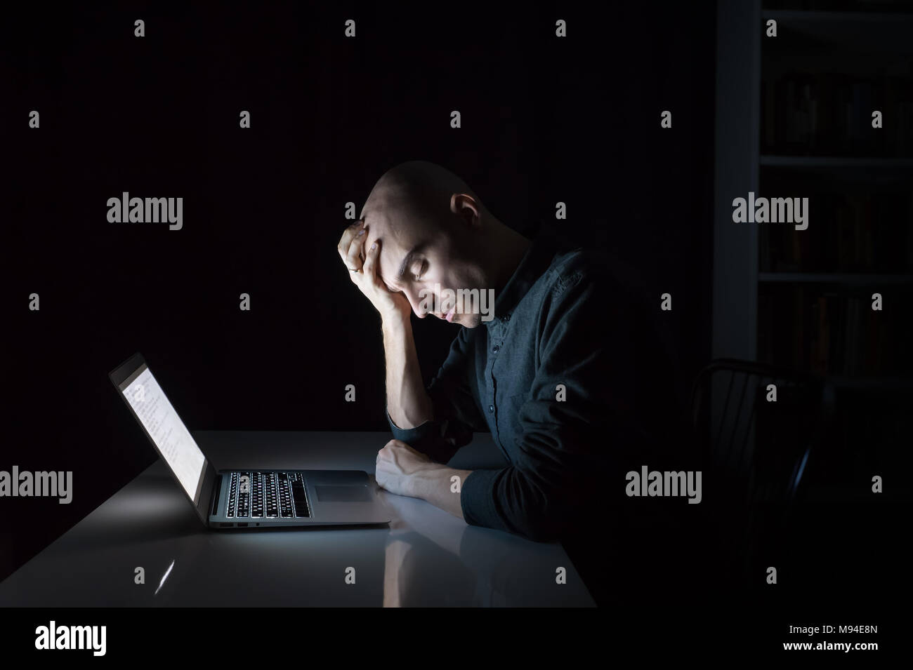 Tired or exhausted man at computer late in the evening with closed eyes. Portrait of young male person working or studying at laptop at night - concep Stock Photo