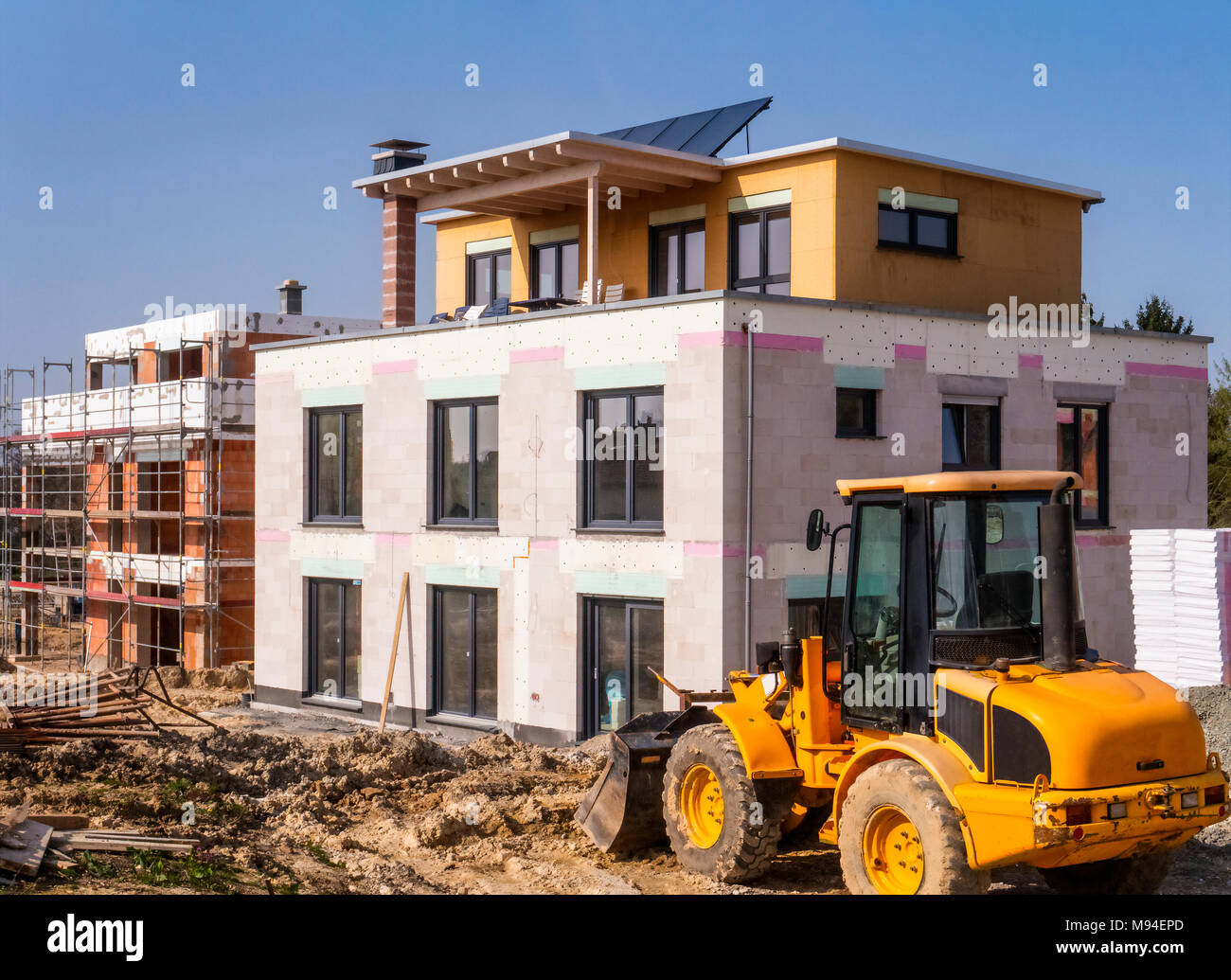 A new building next to a shell in a construction area with a wheel loader in the foreground Stock Photo