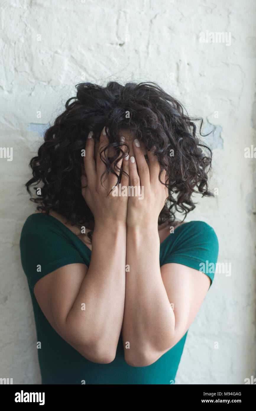 Young woman with dark curlyhair hiding face with hands crying Stock Photo