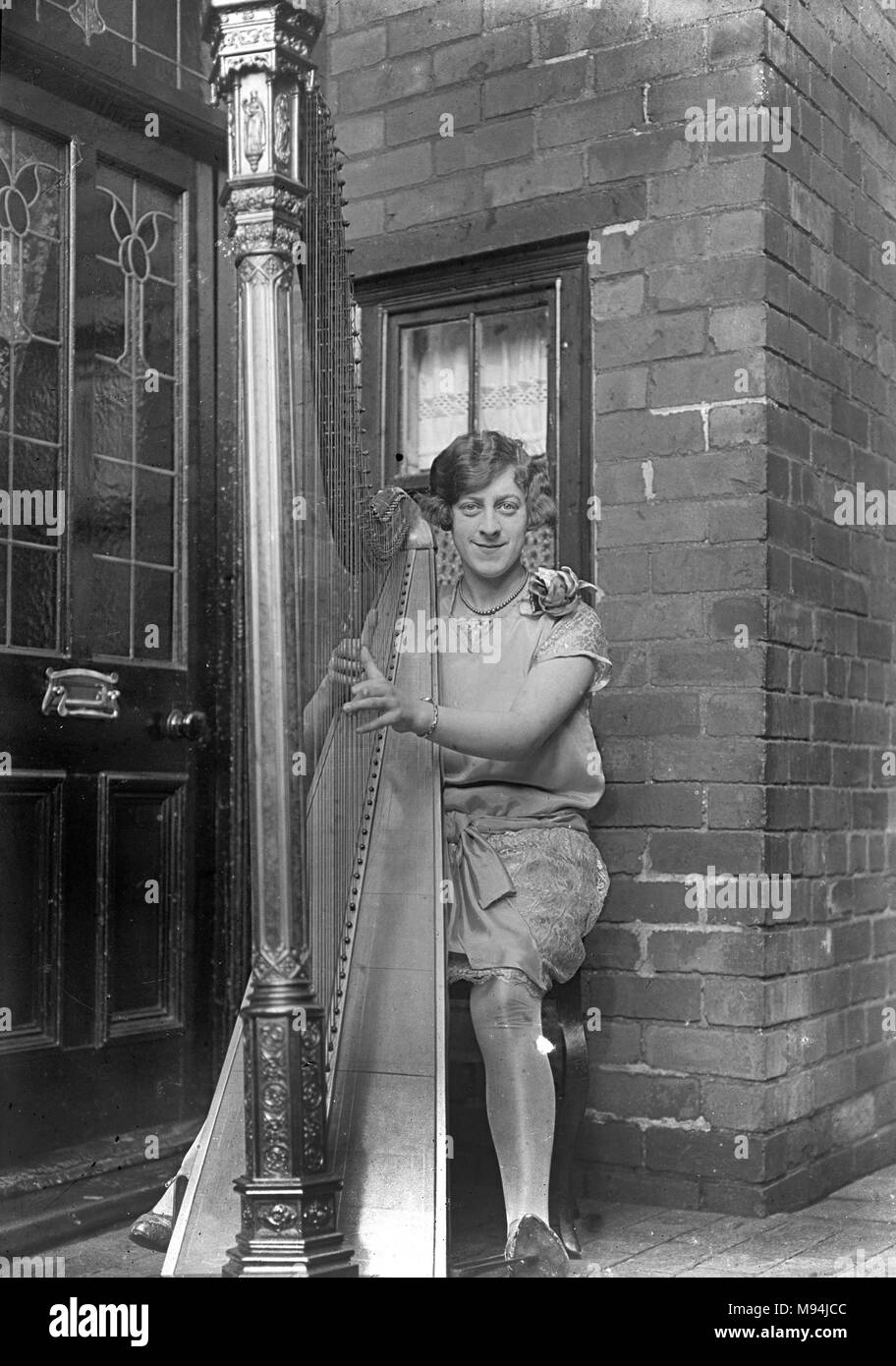 A harpist in England poses with her instrument outside her door, ca. 1910. Stock Photo