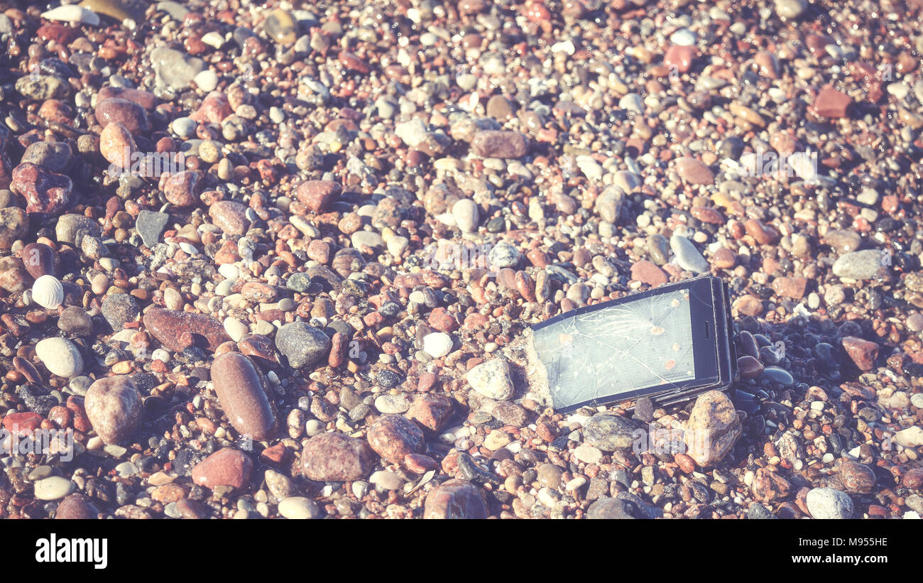 Broken mobile phone with cracked screen on a stony beach, selective focus, color toned picture. Stock Photo