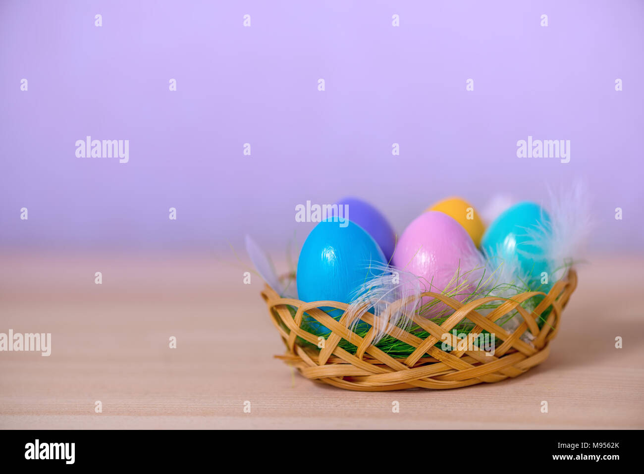 multicolored painted Easter eggs lie in basket with feathers, copy space Stock Photo