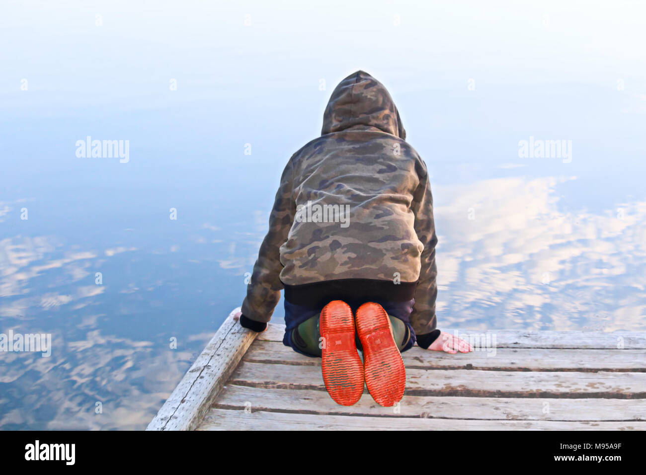 A child looking into water with a mirror reflection of the sky. Stock Photo