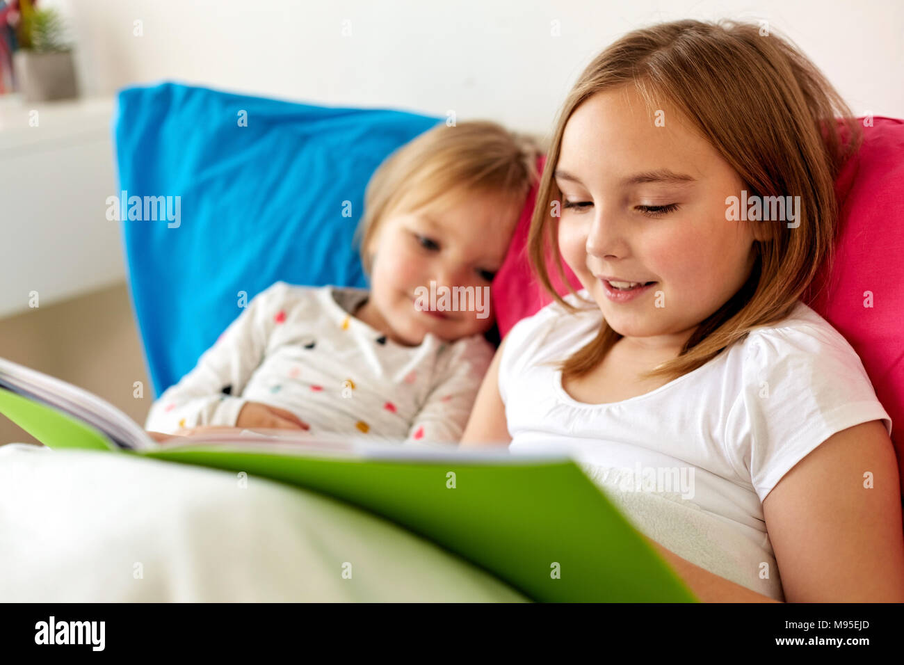 little girls or sisters reading book in bed Stock Photo