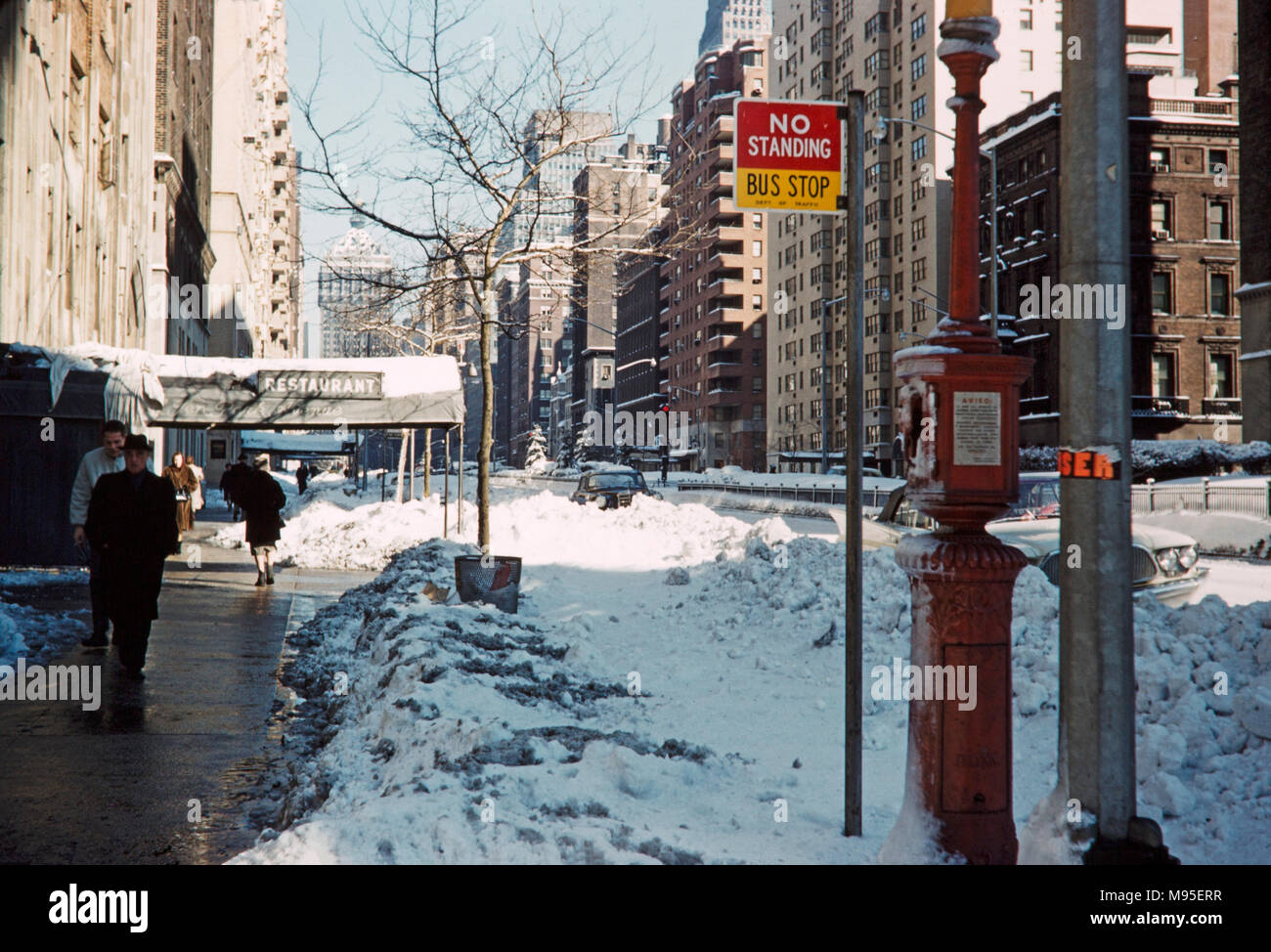 Park Avenue in New York City during a winter in the 1970s. Shows people and buildings on a bright sunny day with snow still at the side of the roads. Stock Photo