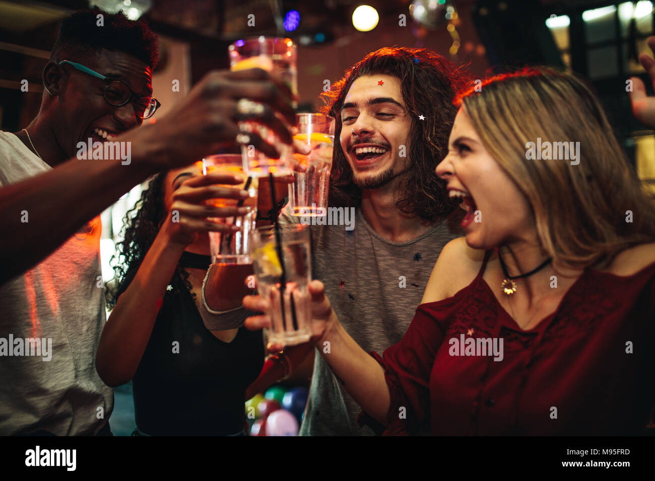 Young men and women celebrating a party, drinking and dancing. Group of friend toasting drinks and having fun at the nightclub. Stock Photo