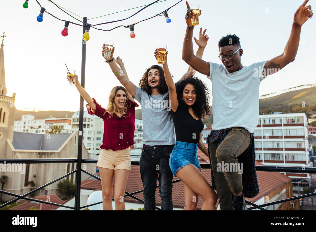 Young people partying on terrace with drinks. Mixed race men and women enjoying drinks on rooftop. Stock Photo