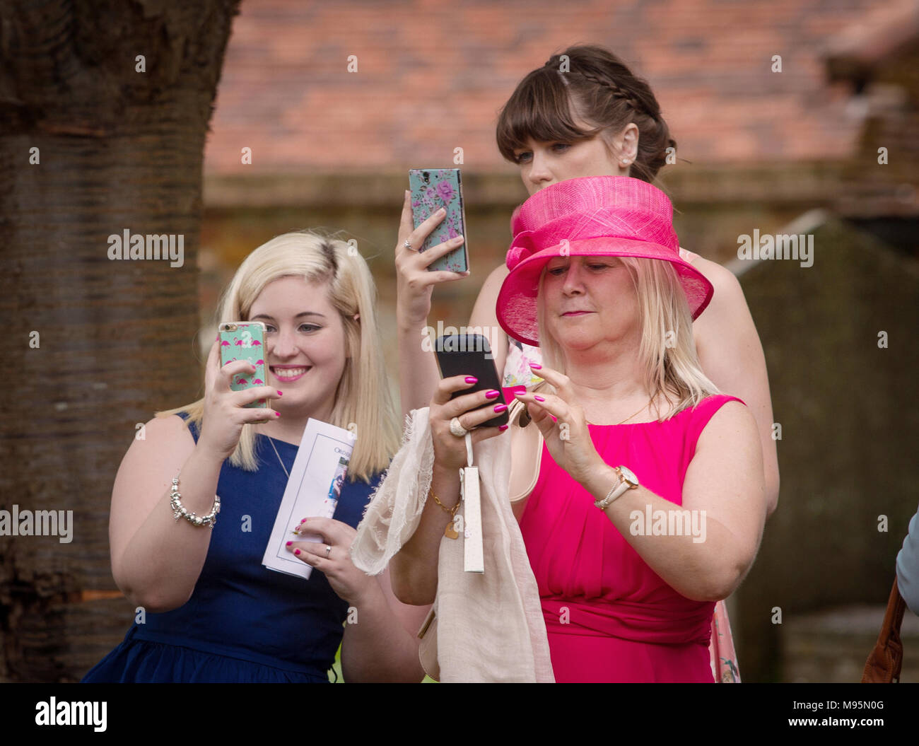 Female guests at wedding taking photographs on mobile phones Stock Photo