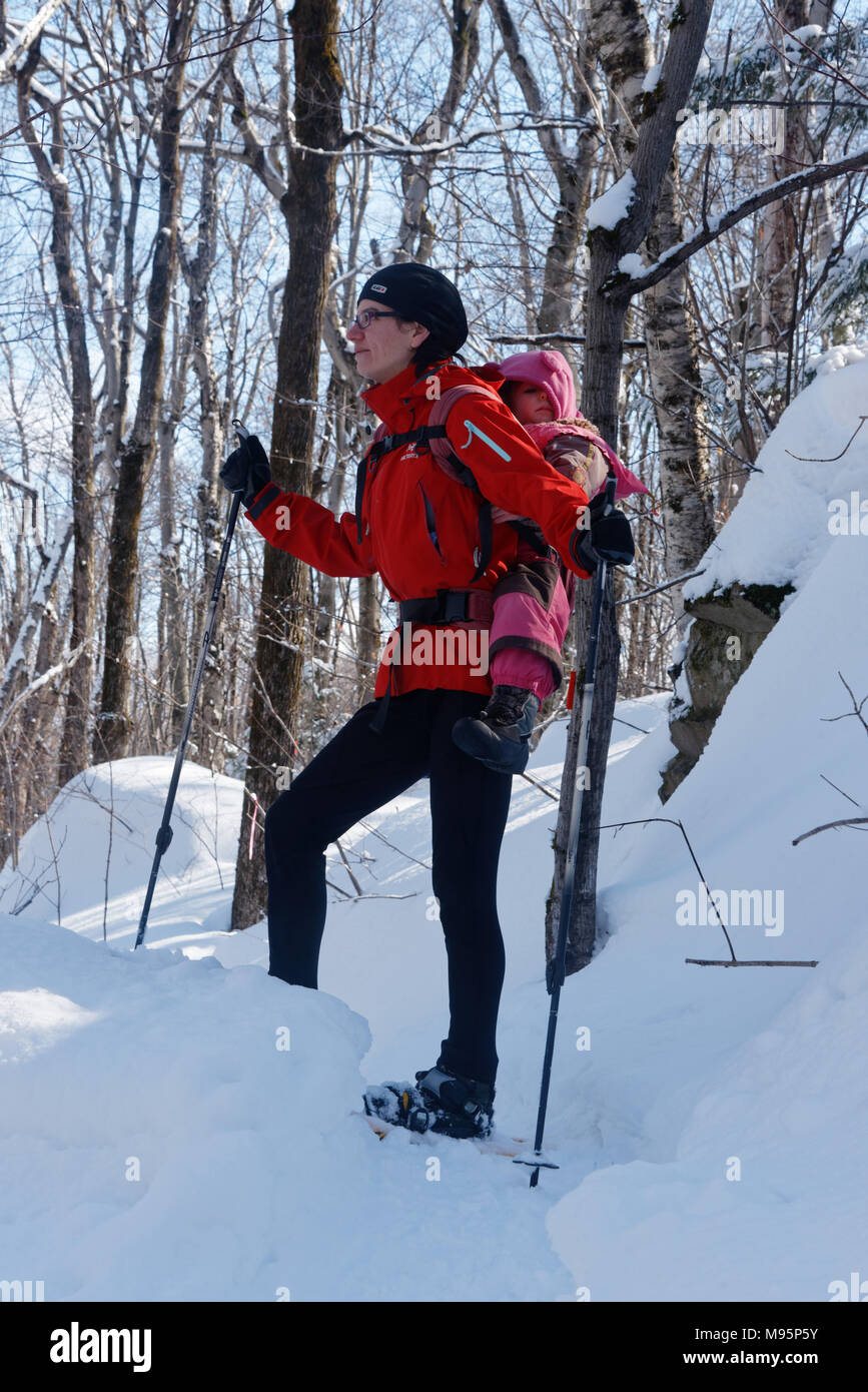 A mother snowshoeing in Quebec Canada with her three year old child on her back Stock Photo