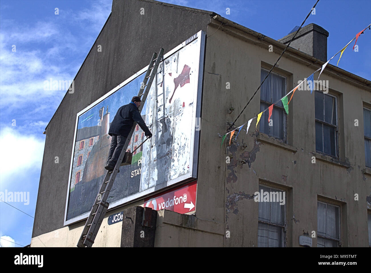 man up a ladder putting up a new advertising hoarding, billboard for jamesons whisky a famous irish whisky. skibbereen, ireland Stock Photo