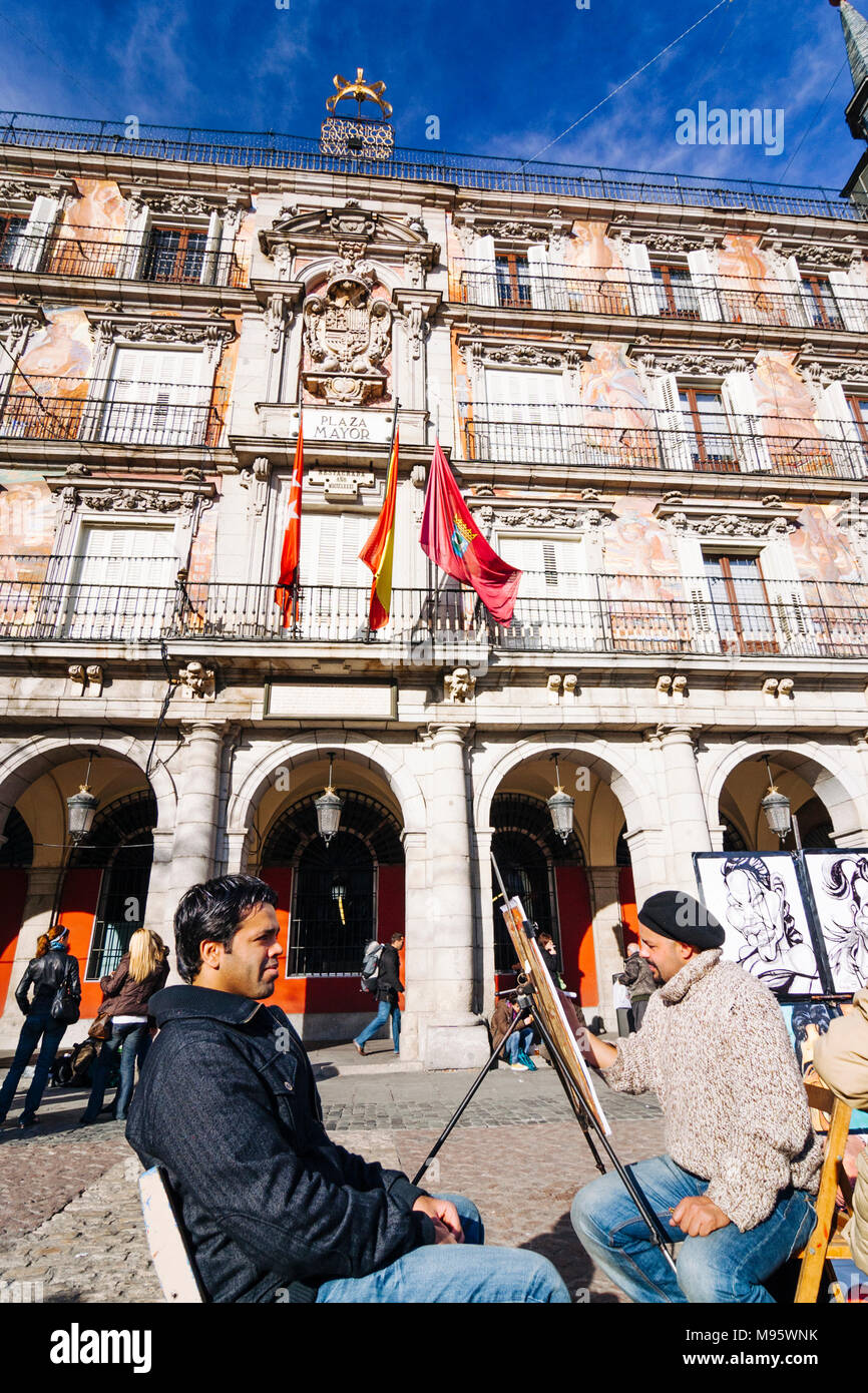 Madrid, Spain : Plaza Mayor square. A street cartoonist draws a caricature of a young man by Casa de la Panadería (Bakery House) designed by Juan de V Stock Photo