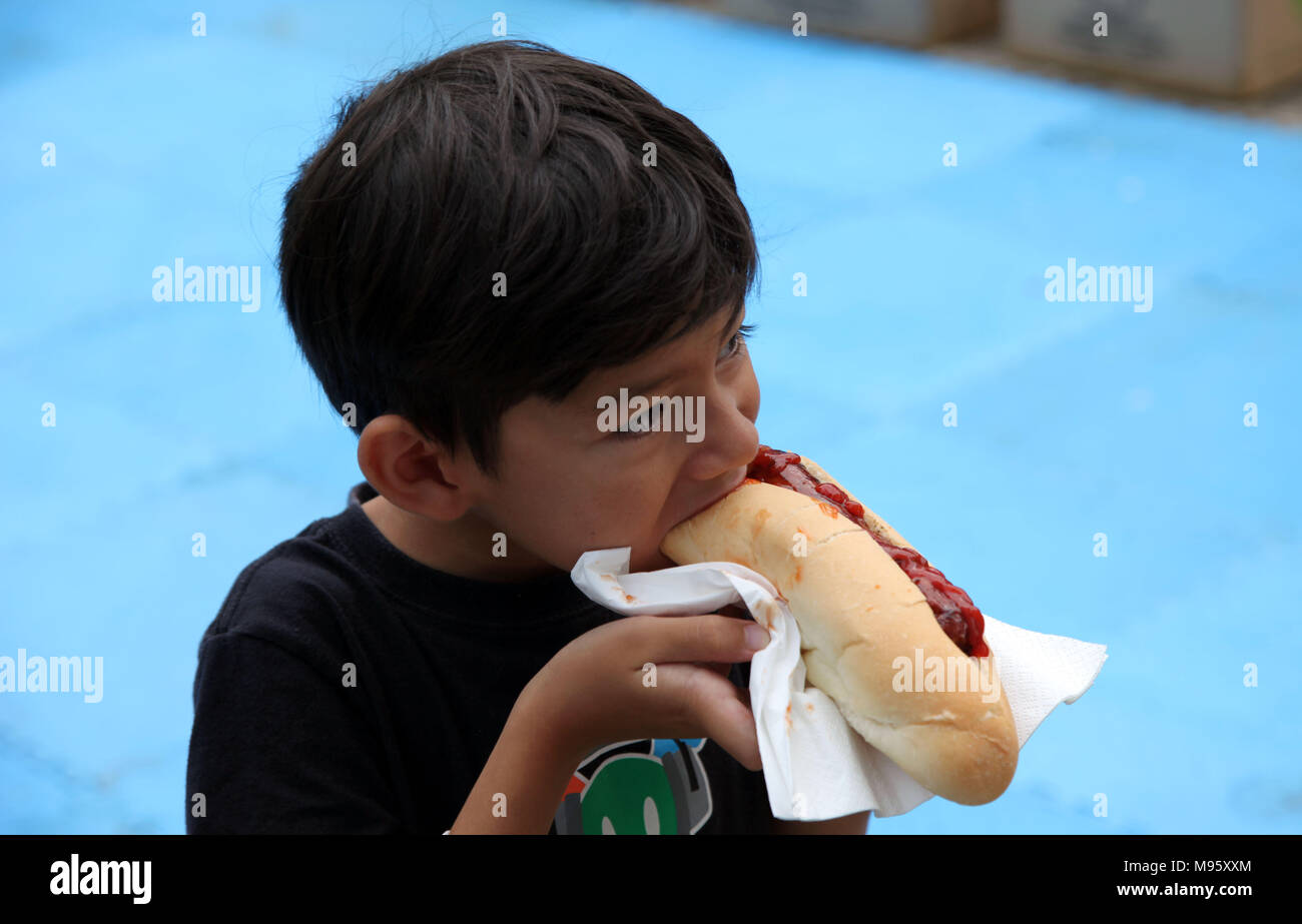 Little HUngry Eurasian Boy Eating a Hot-dog with appetite Stock Photo