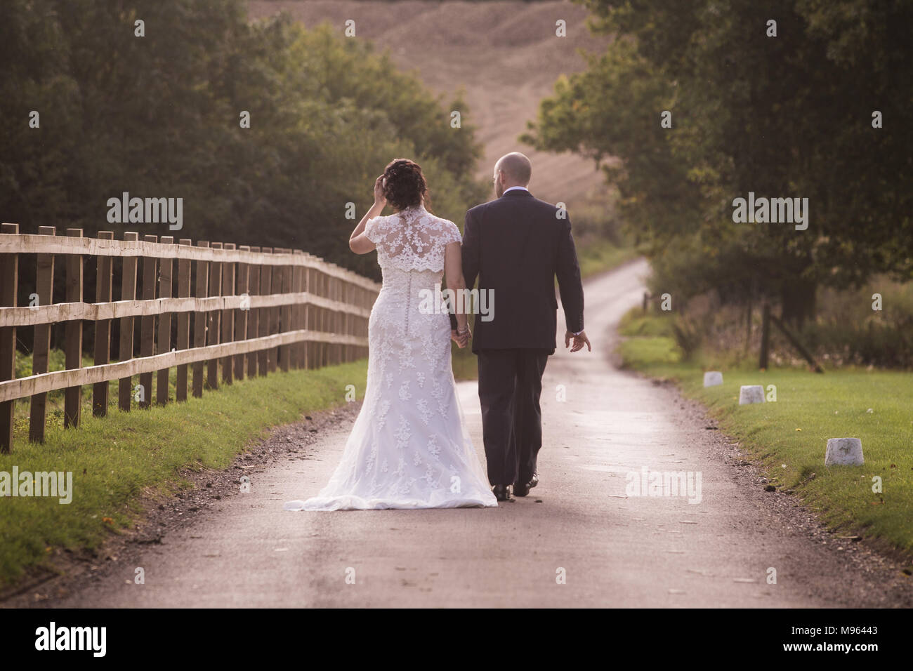 newly married couple walking hand in hand down country lane Stock Photo