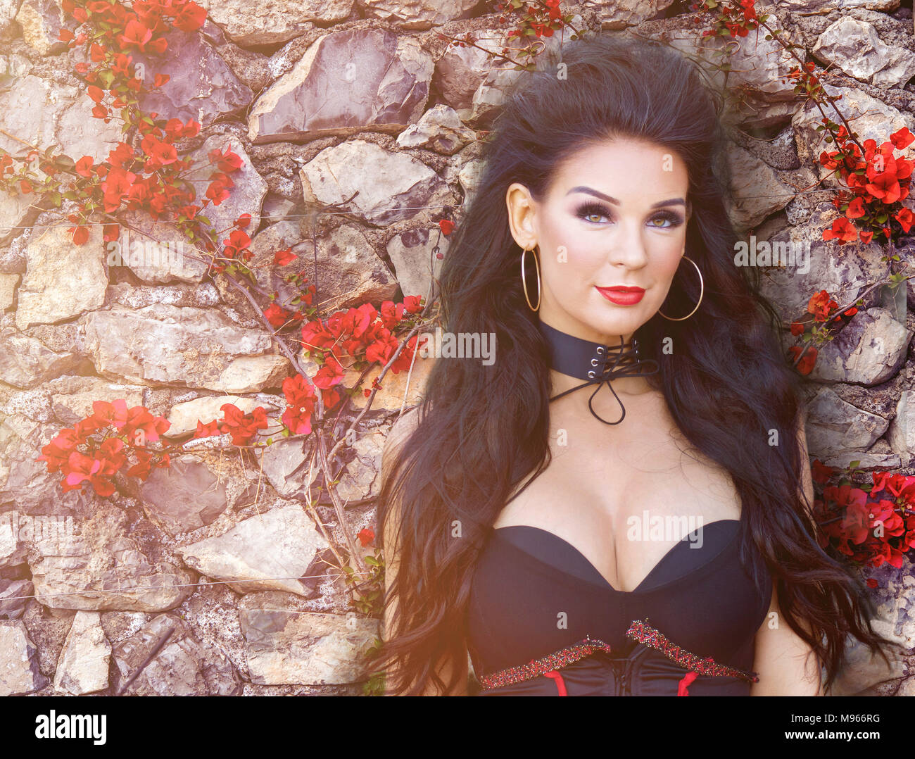 Beautiful Spanish woman against a rock wall with brilliant red bougainvillea flowers surrounding her Stock Photo