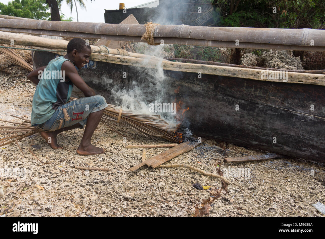 A boat builder using traditional methods burning a wooden dug out boat to seal it and make it water tight on Zanzibar island Stock Photo