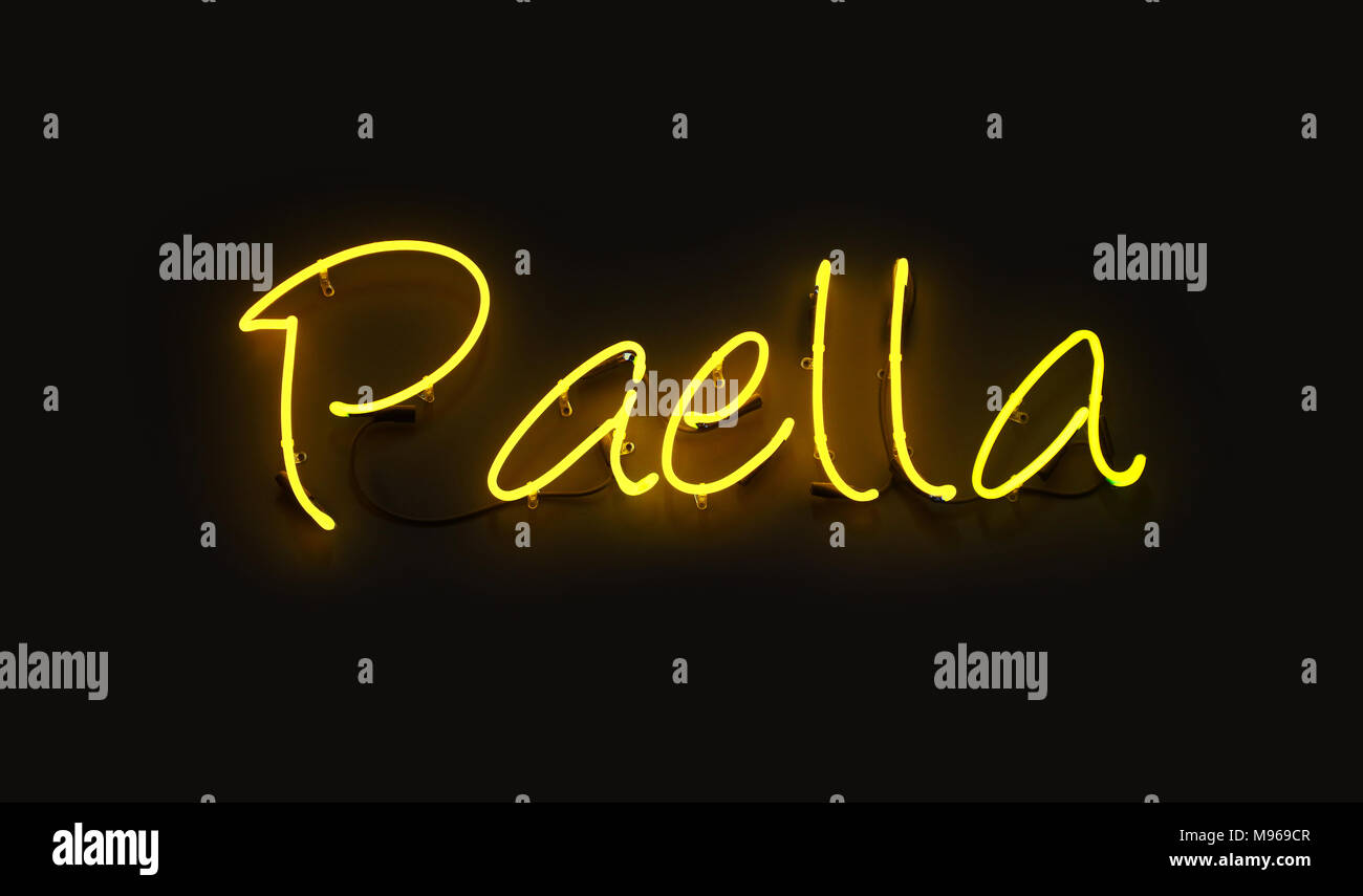 Close up PAELLA yellow neon light sign glowing in the dark over black wall background Stock Photo