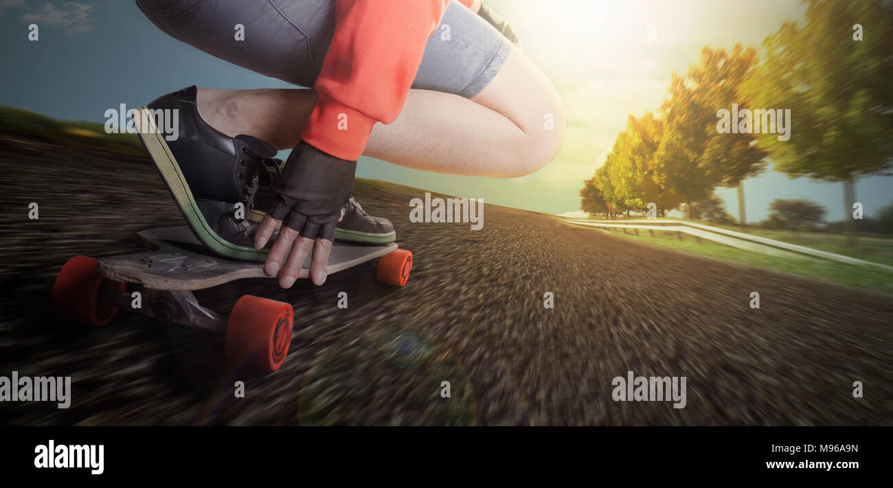 Man rides on a longboard in the street of a countryside environment with trees and blue sky. He drives with high speed experiencing the danger Stock Photo