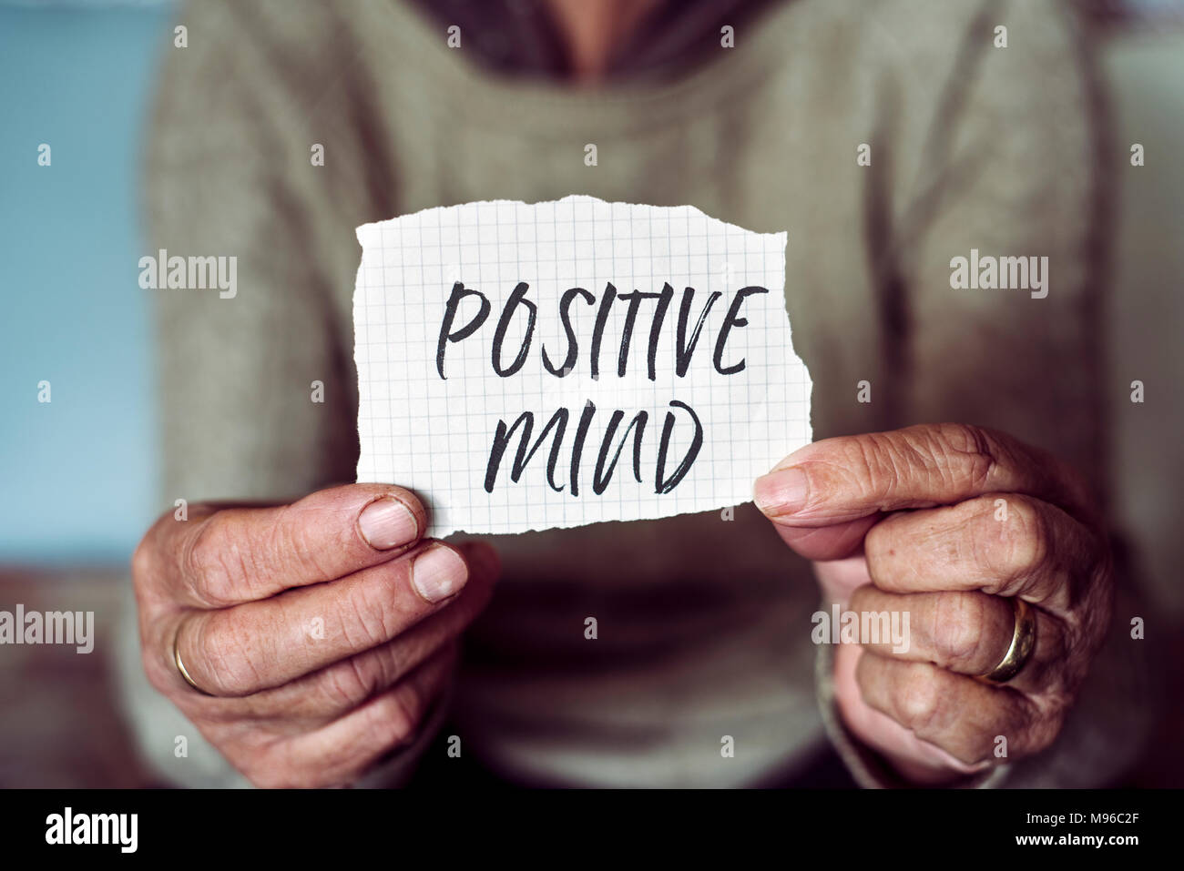 closeup of an old caucasian woman showing a note with the text positive mind written in it Stock Photo