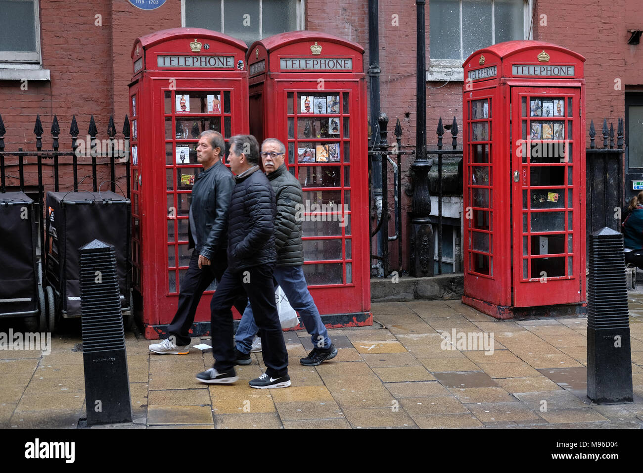 Three tourists walking past London telephone boxes. Stock Photo