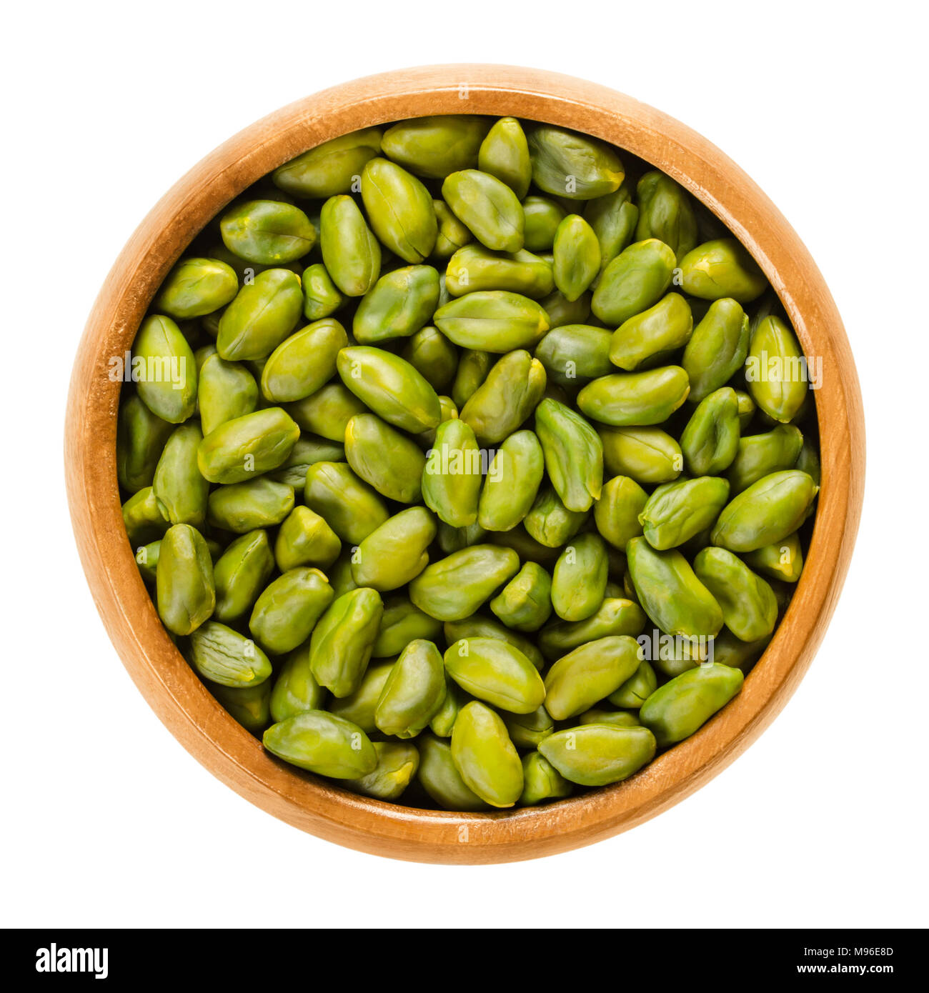 Green pistachios in wooden bowl. Dried and peeled kernels. Shelled fruits and seeds of Pistacia vera. Used as snack and for desserts. Stock Photo