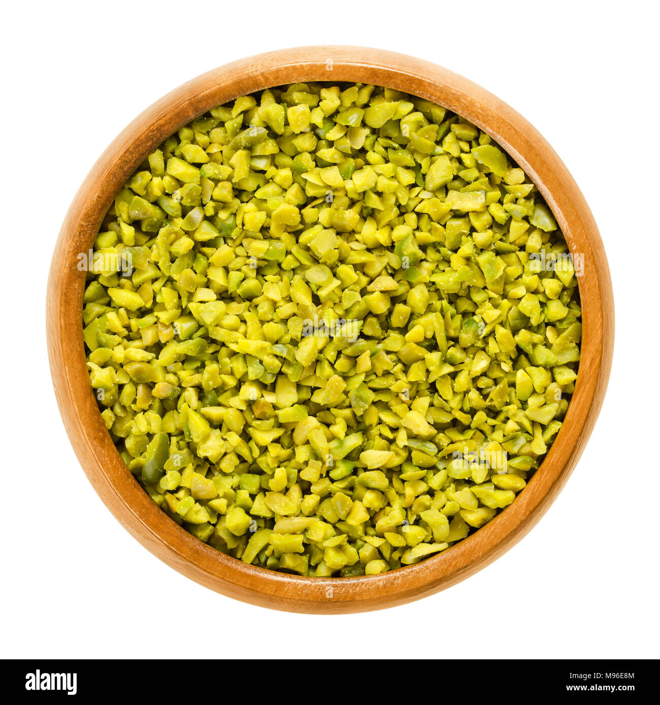 Chopped green pistachios in wooden bowl. Dried and peeled kernels. Shelled fruits and seeds of Pistacia vera. Used as snack or for desserts. Stock Photo