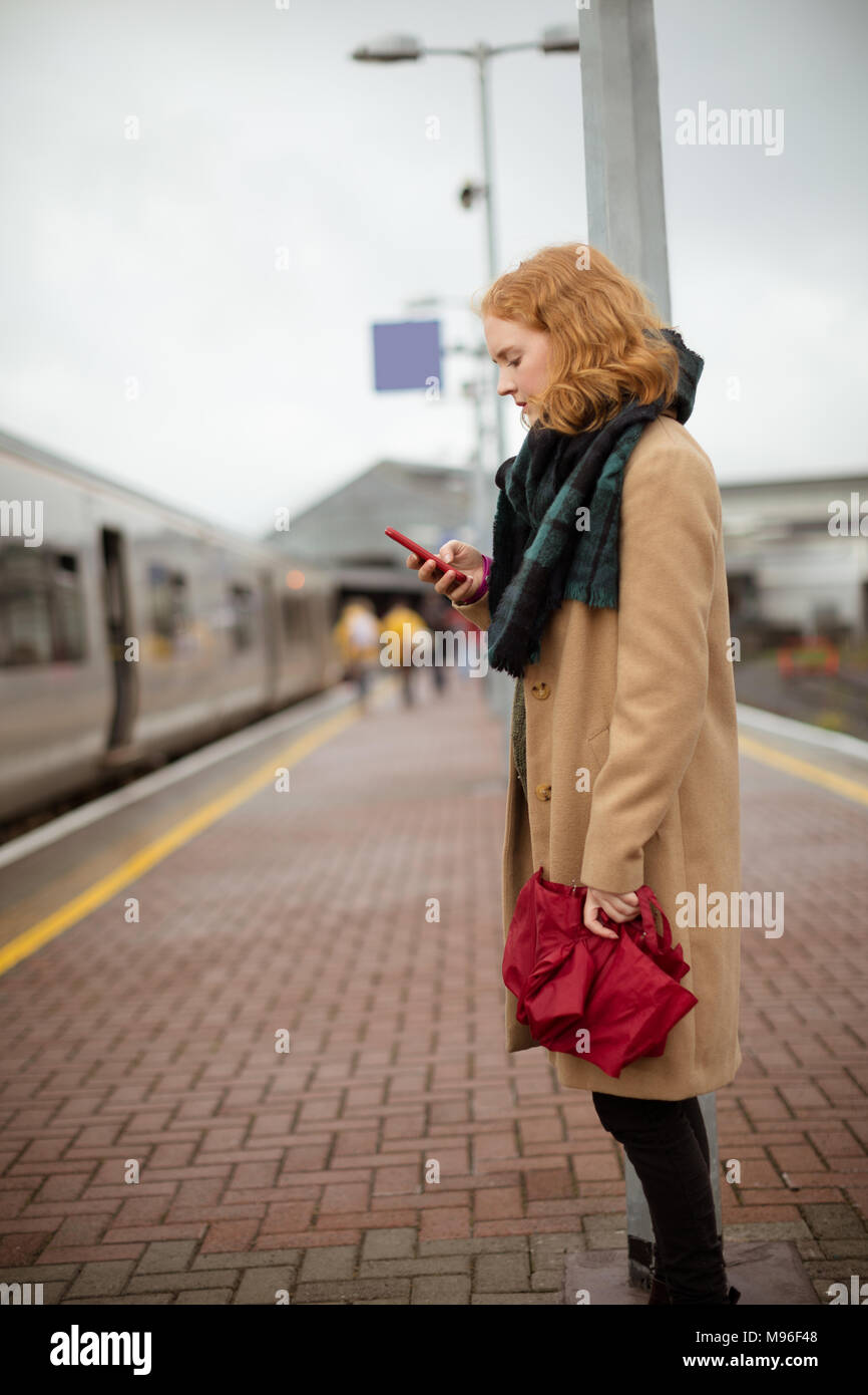 Young woman standing on railway platform using her mobile phone Stock Photo